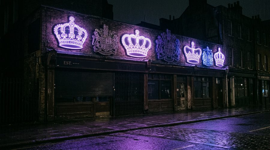 Deretan lampu neon berbentuk mahkota dan lambang menyala ungu di atas toko gelap malam hari